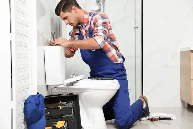 A plumber is fixing a toilet in a bathroom.