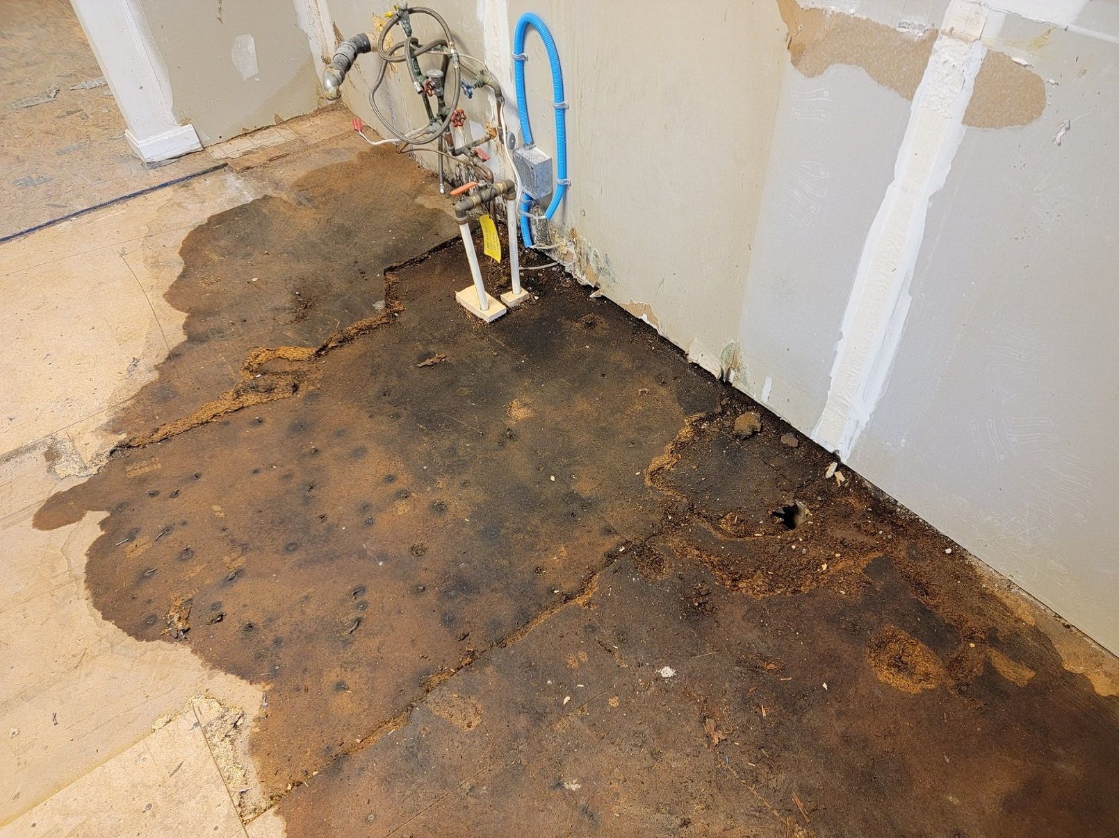 A dirty floor in a room with a blue pipe coming out of the wall.
