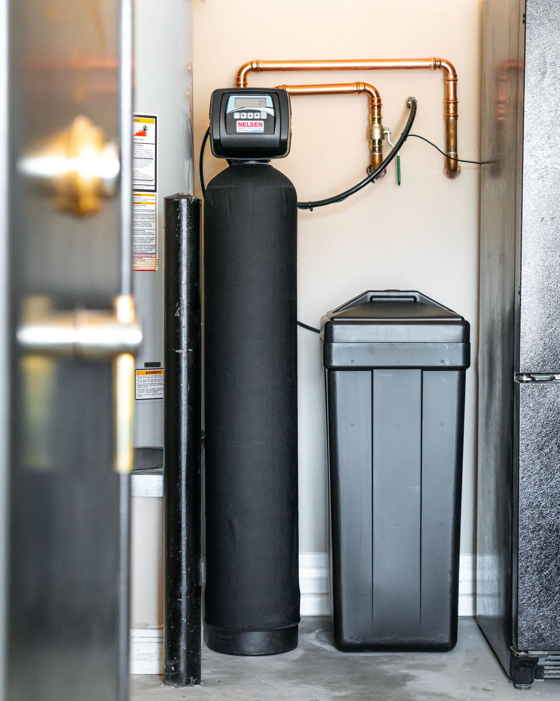 A water softener is sitting in a garage next to a refrigerator.