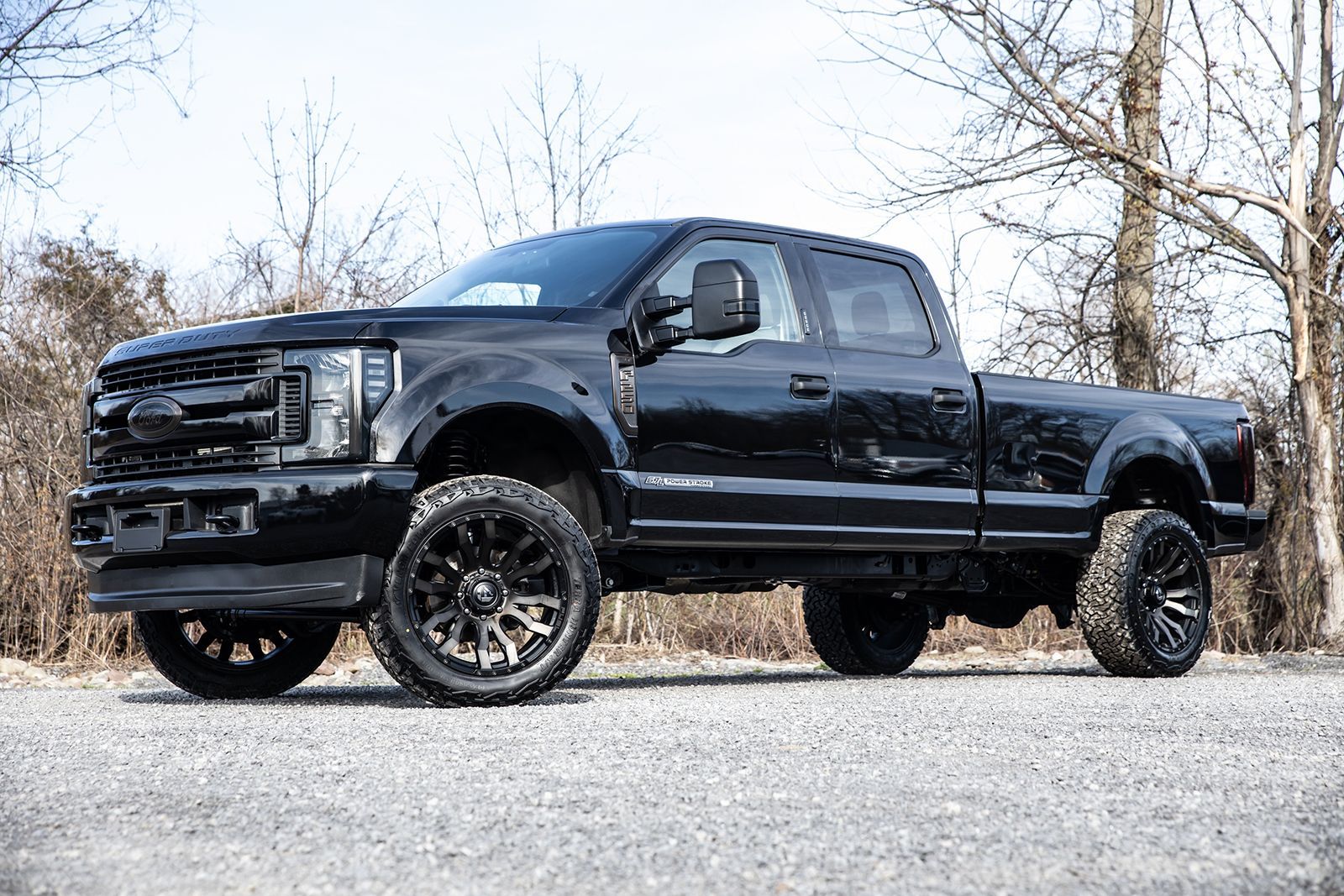 Black lifted Ford pickup truck with custom wheels parked on gravel.