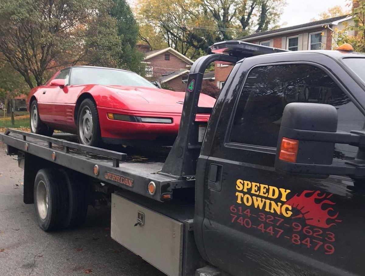 A red corvette is being towed by a speedy towing truck.