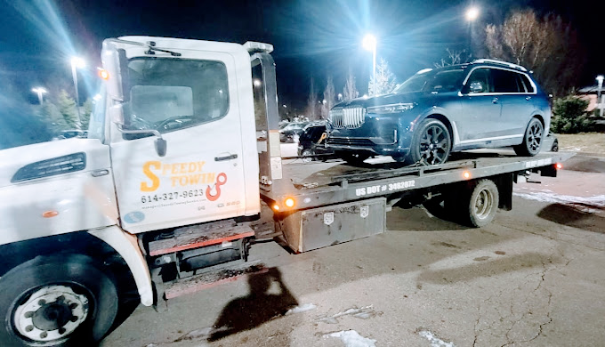 A car is being towed by a tow truck at night.