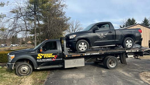 A black truck is being towed by a tow truck.