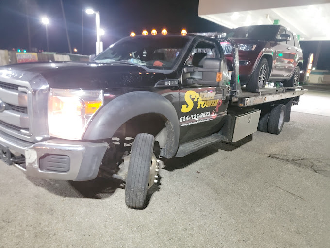 A tow truck with a car on the back is parked in a parking lot.