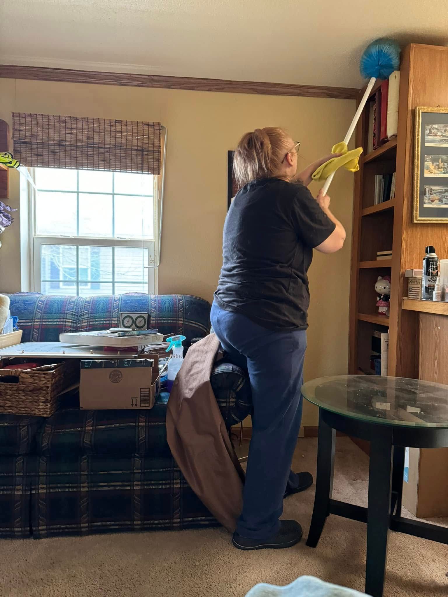Person reaching for something on a high shelf with a grabbing tool. They are inside, near a window and bookshelf.