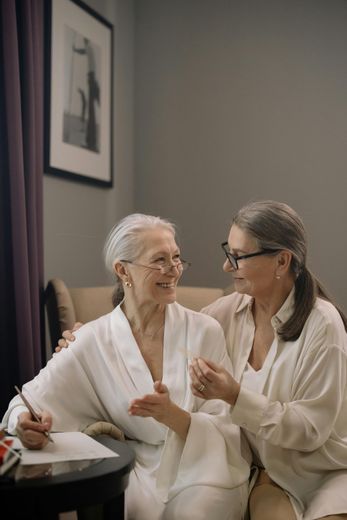 Two elderly women are sitting on a couch talking to each other.