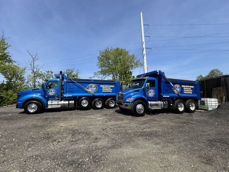 Two blue dump trucks are parked next to each other in a parking lot.