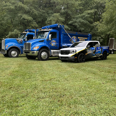 Two blue trucks and a white truck are parked in a grassy field.