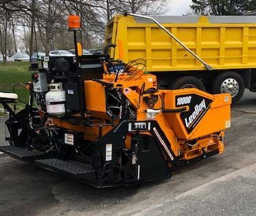 A yellow dump truck is parked next to a yellow asphalt paving machine.
