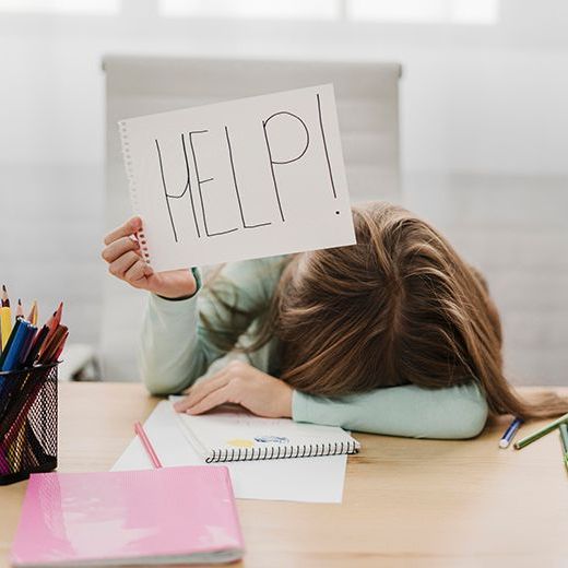 Ein Mädchen sitzt an einem Schreibtisch und hält ein Schild mit der Aufschrift „Hilfe“. Lernprobleme