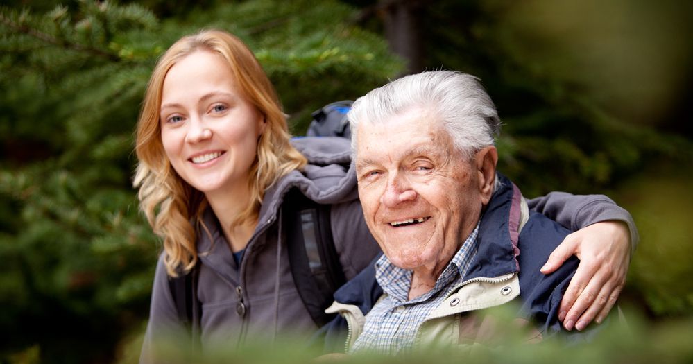 Betreuerin mit älterem Mann im Rollstuhl.