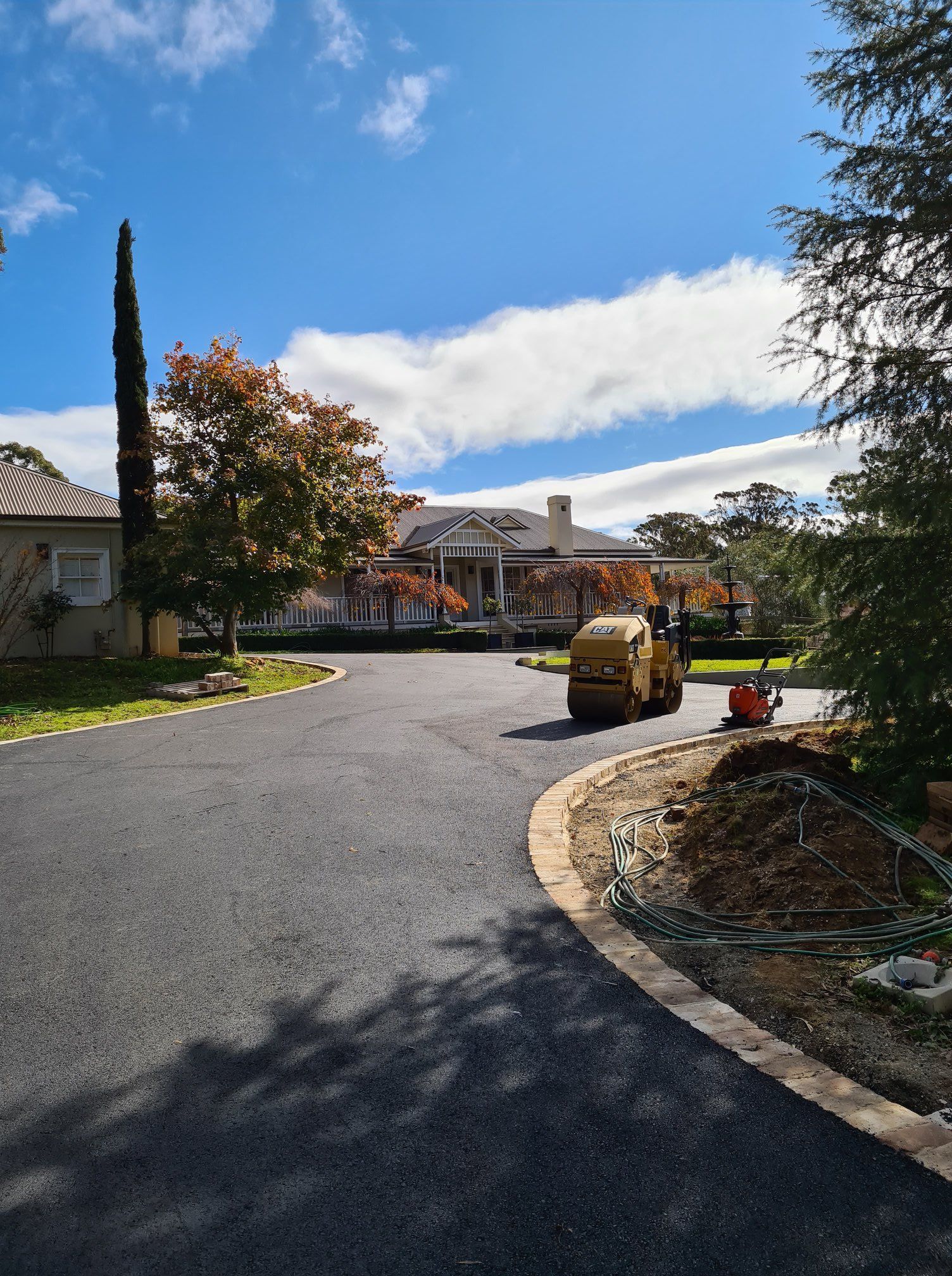 A Road Is Being Paved In Front Of A House On A Sunny Day — About Time Plumbing & Civil Construction in Moss Vale, NSW