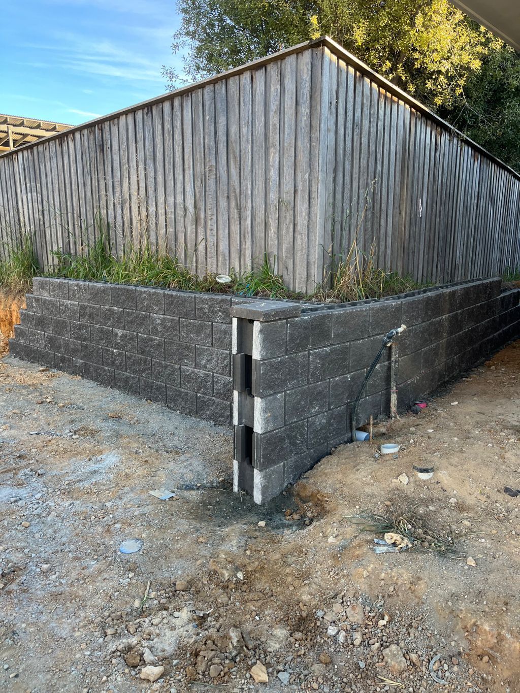 A Brick Wall Is Being Built Next To A Wooden Fence — About Time Plumbing & Civil Construction in Moss Vale, NSW