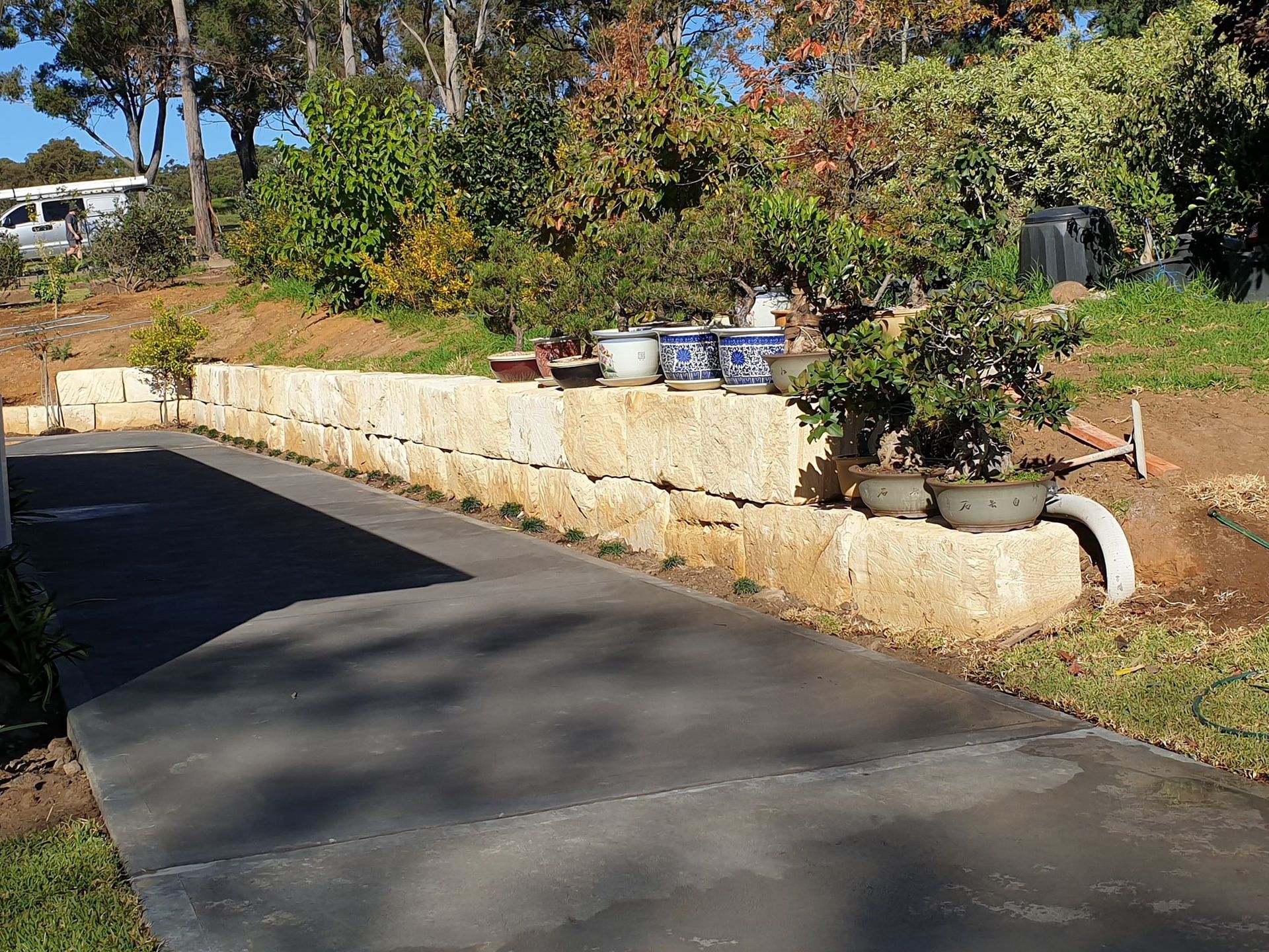 A Driveway With A Stone Wall And Potted Plants On It — About Time Plumbing & Civil Construction in Moss Vale, NSW