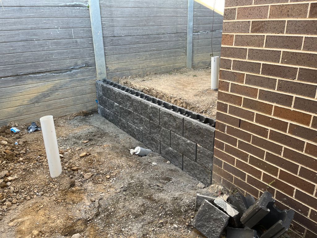 A Brick Wall Is Being Built Next To A Fence — About Time Plumbing & Civil Construction in Moss Vale, NSW