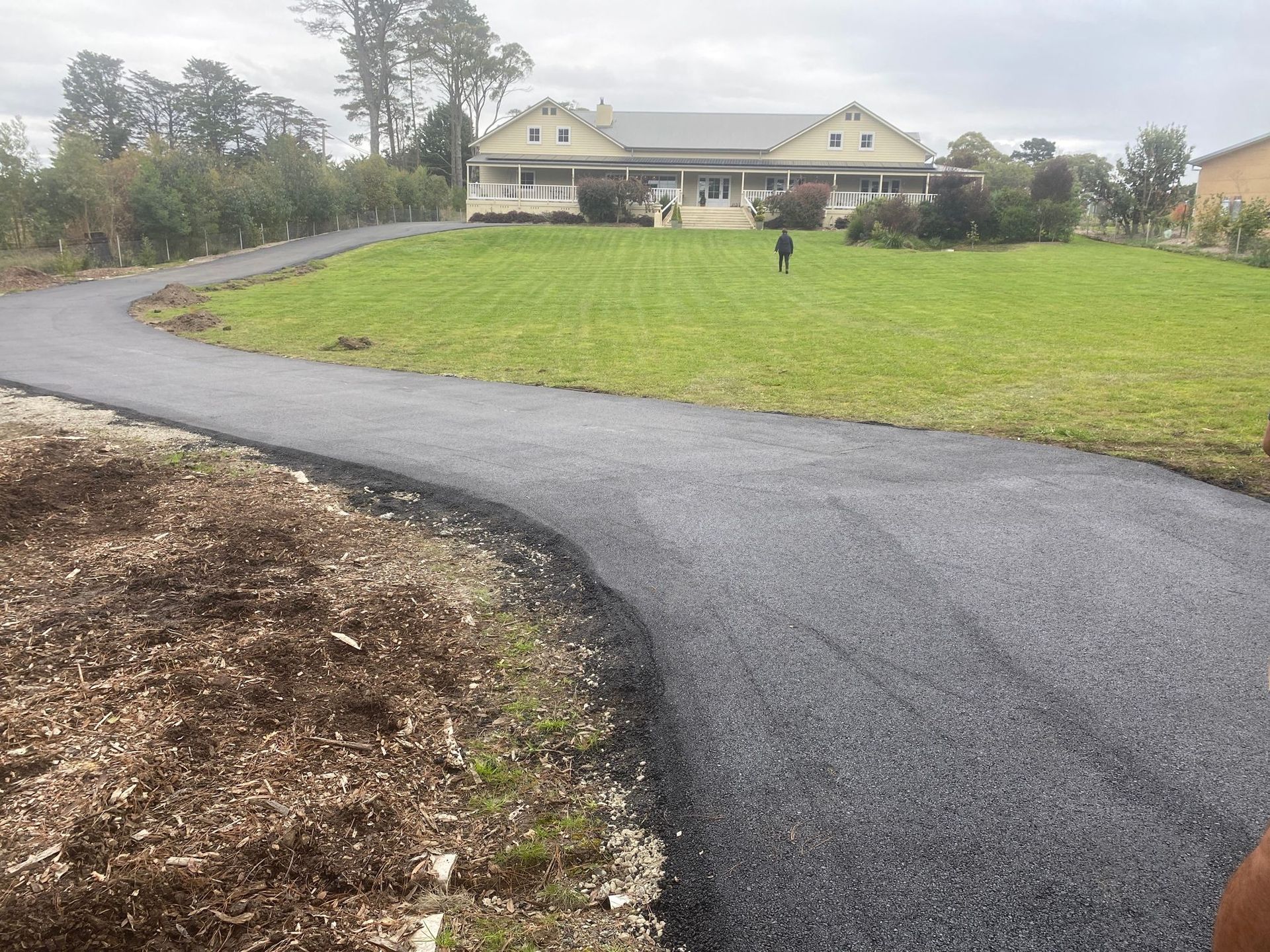 A Person Is Walking Down A Road In Front Of A Large House — About Time Plumbing & Civil Construction in Moss Vale, NSW