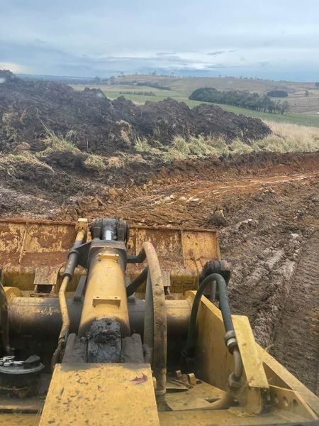 A Bulldozer Is Moving Dirt In A Field With Mountains In The Background — About Time Plumbing & Civil Construction in Bowral, NSW