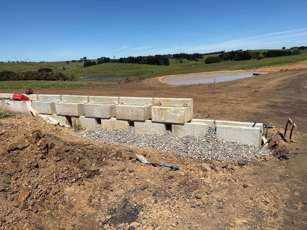 A Concrete Wall Is Being Built In A Dirt Field With A Pond In The Background — About Time Plumbing & Civil Construction in Moss Vale, NSW