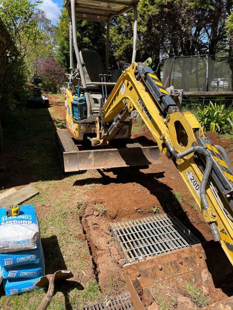 Yellow Excavator Next to Drainage — About Time Plumbing & Civil Construction in Moss Vale, NSW