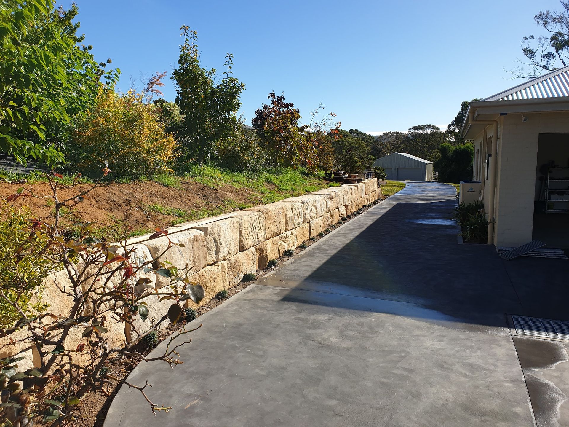 A Driveway Leading To A House With A Stone Wall Along The Side Of It — About Time Plumbing & Civil Construction in Moss Vale, NSW