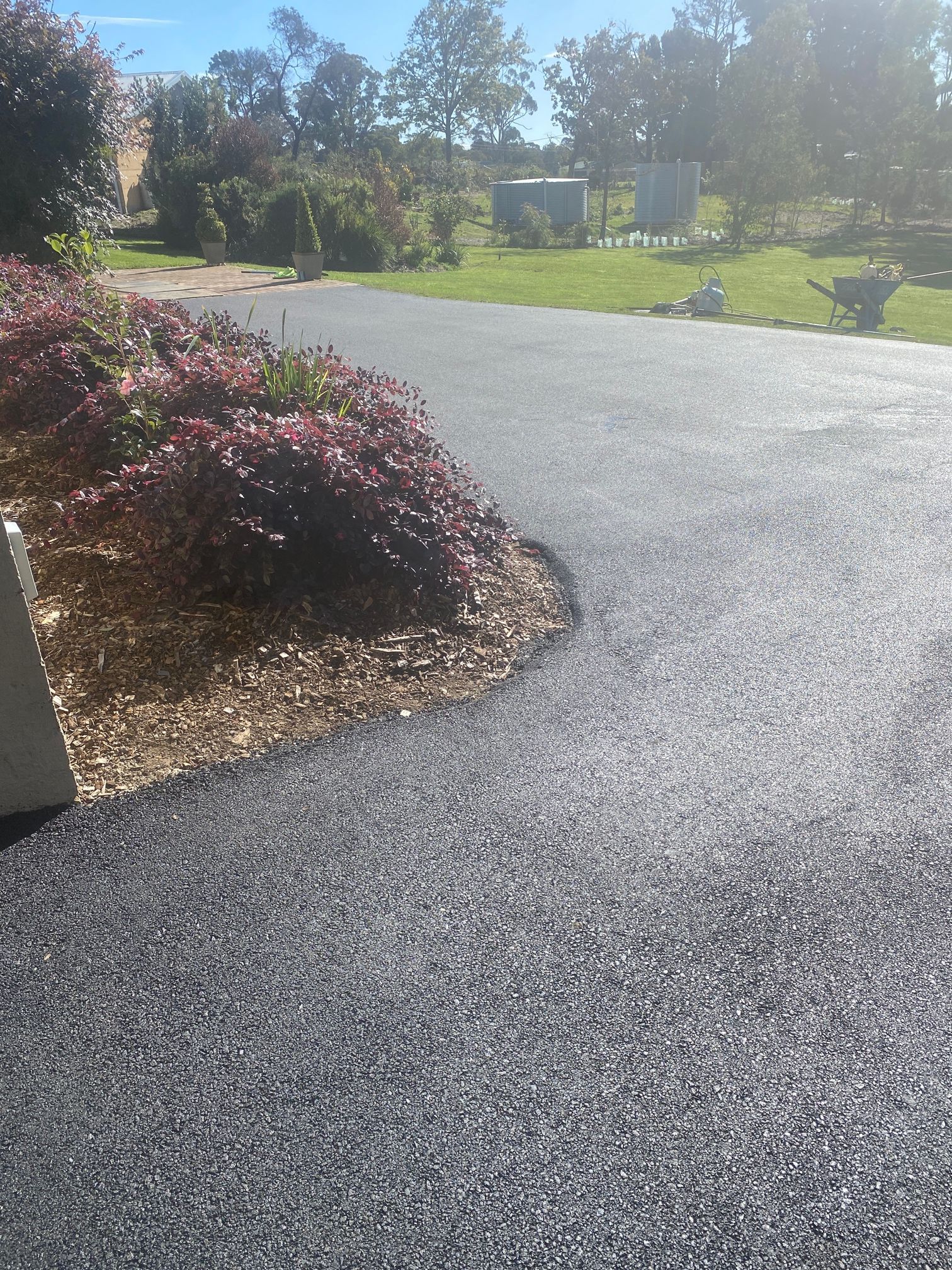 A Black Asphalt Driveway With A Bush In The Middle Of It — About Time Plumbing & Civil Construction in Moss Vale, NSW