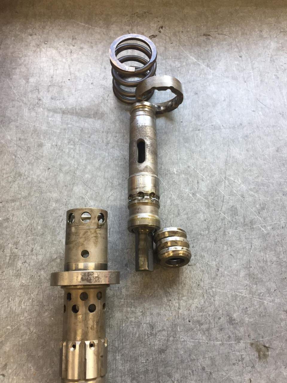 Disassembled metal industrial components: a spring, a long shaft, and two cylindrical parts with holes.