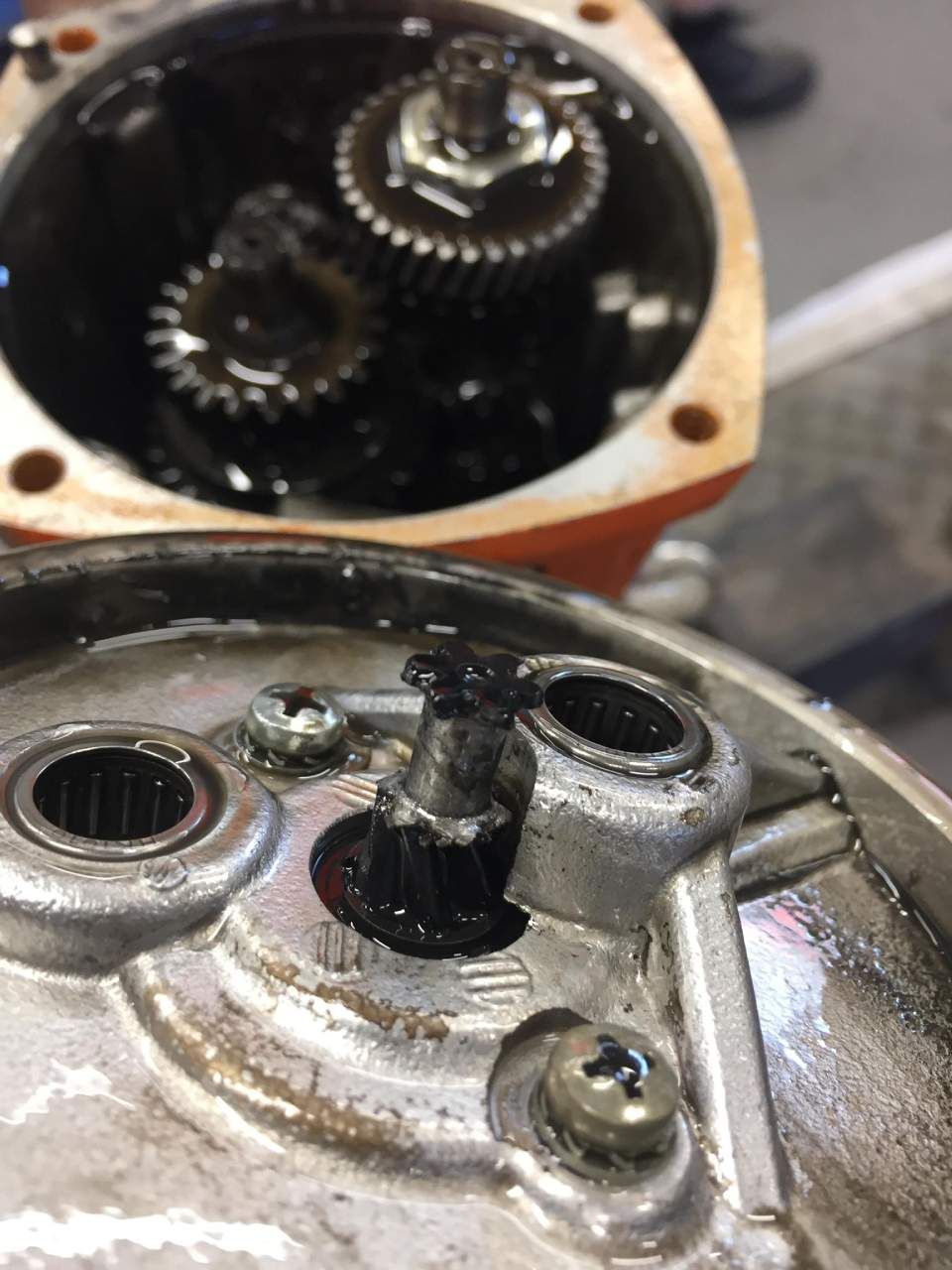 Gearbox components disassembled, showing gears and mounting brackets. Dark oil present.