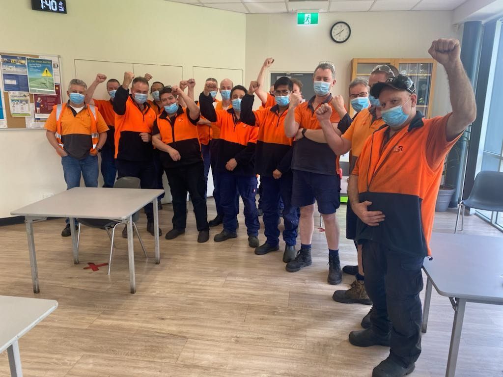 Group of people in orange shirts and masks, raising fists in a room, celebrating.