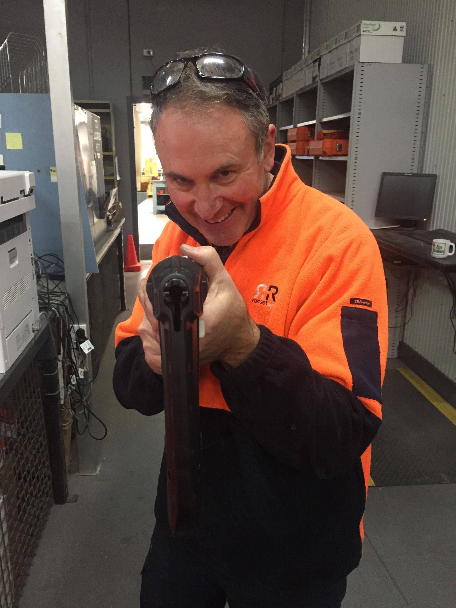 Man in orange workwear smiling, holding a dark object, indoors.