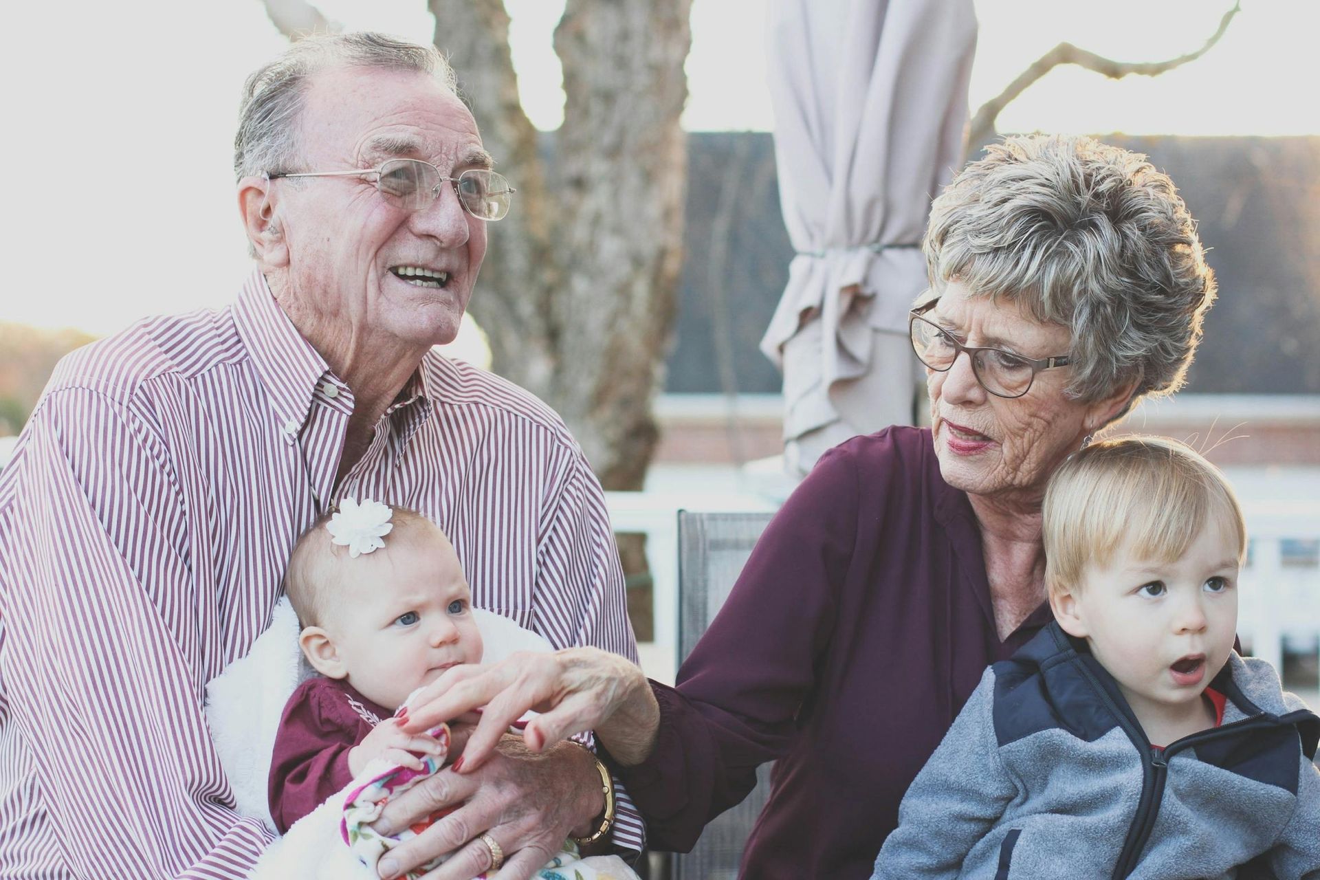 Grandparents seated outdoors with two young grandchildren; talking and smiling.