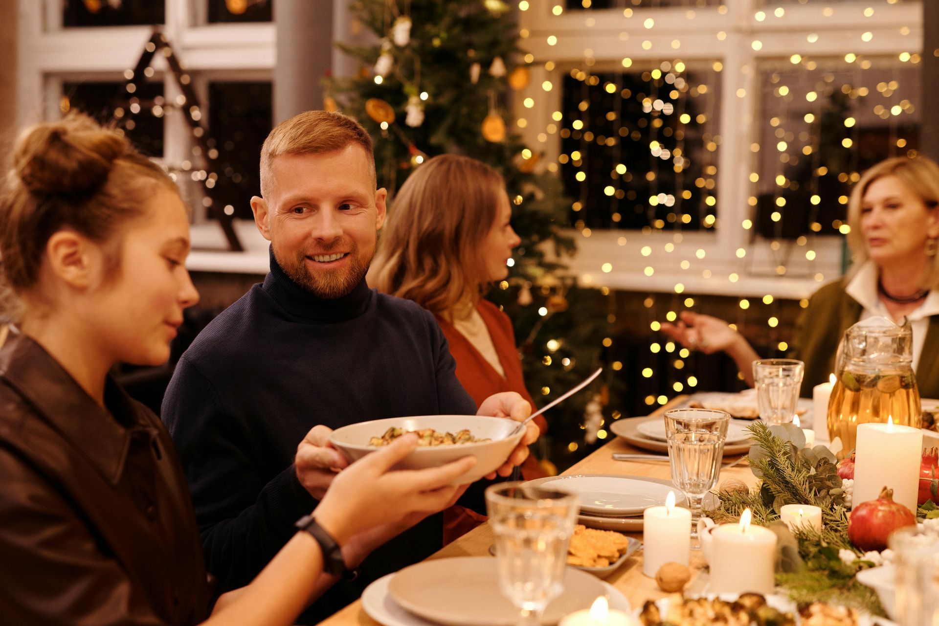 Family sharing food at a festive dinner table, lit by candles and fairy lights.