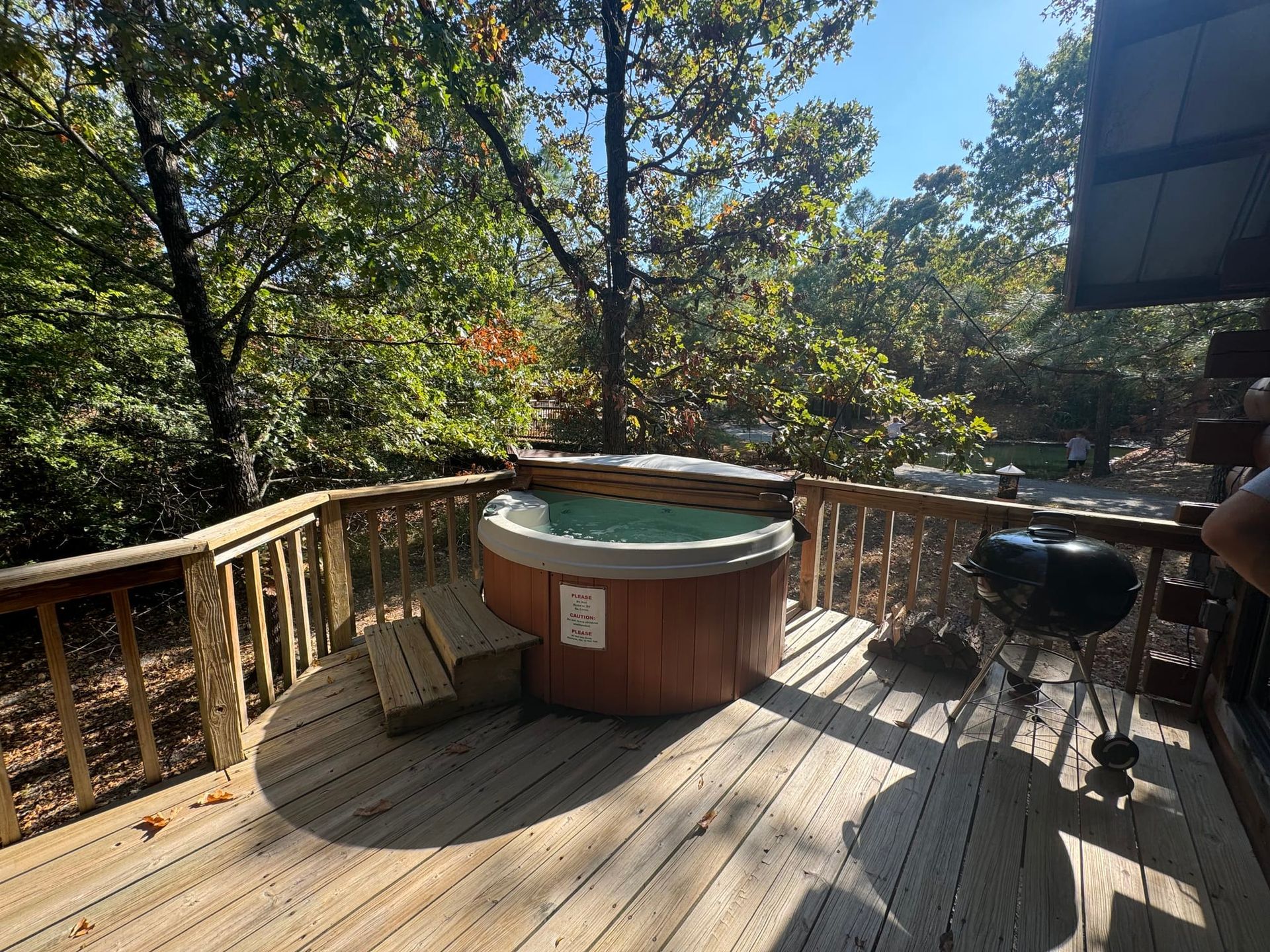 A hot tub is on a wooden deck with trees in the background.