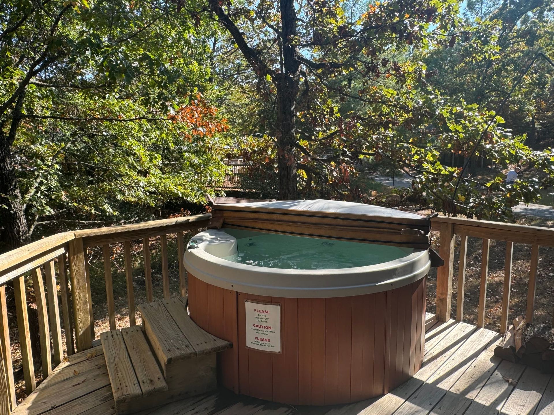 A hot tub is sitting on a wooden deck surrounded by trees.