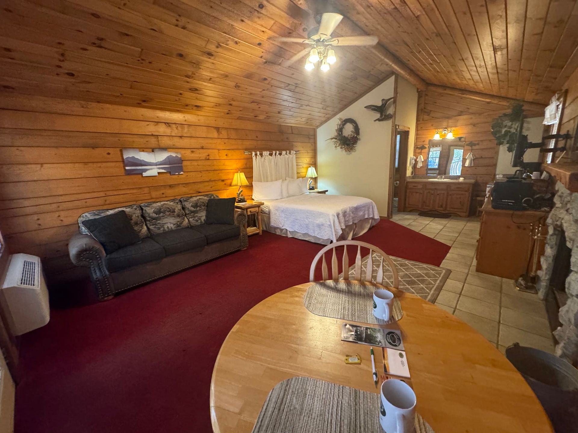A living room in a log cabin with a bed , couch , table and fireplace.