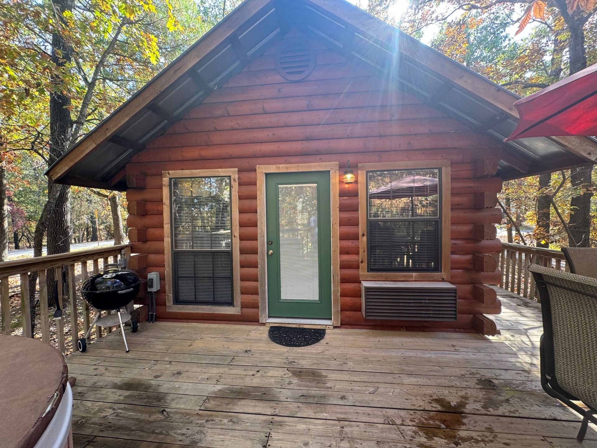 A small log cabin with a green door and a hot tub on the deck.