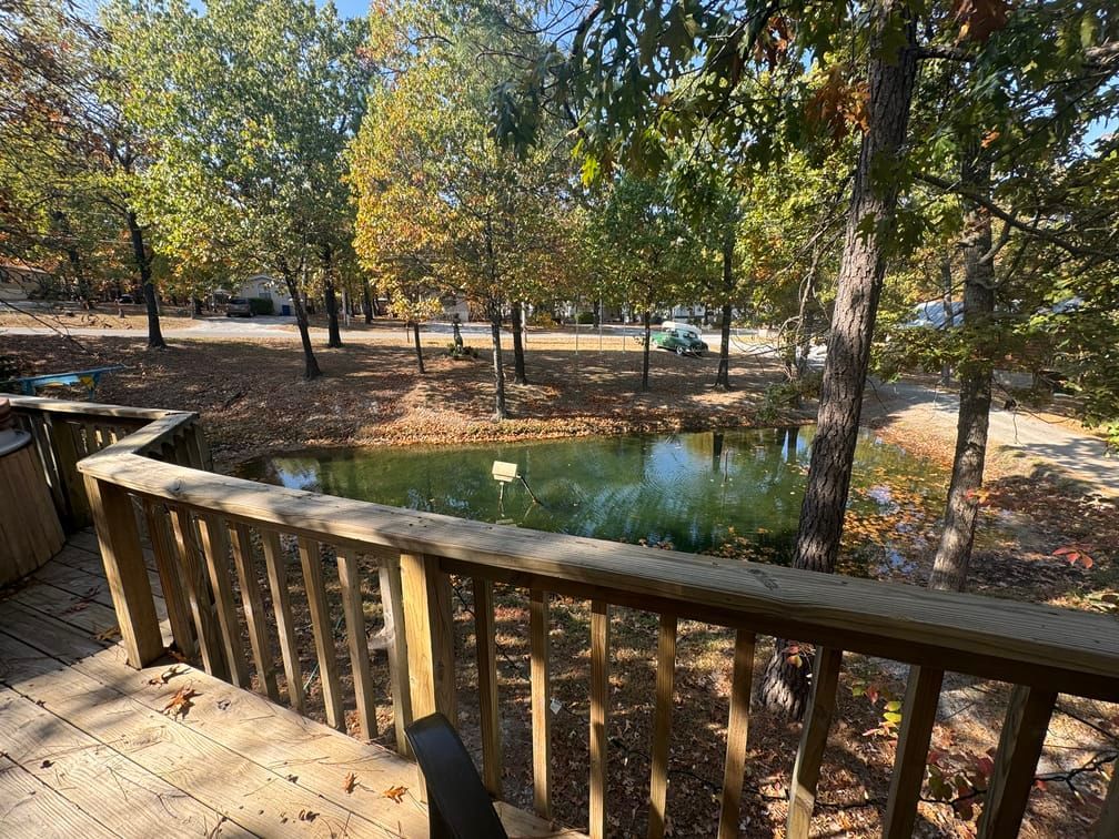 A wooden deck overlooking a pond in the middle of a forest.