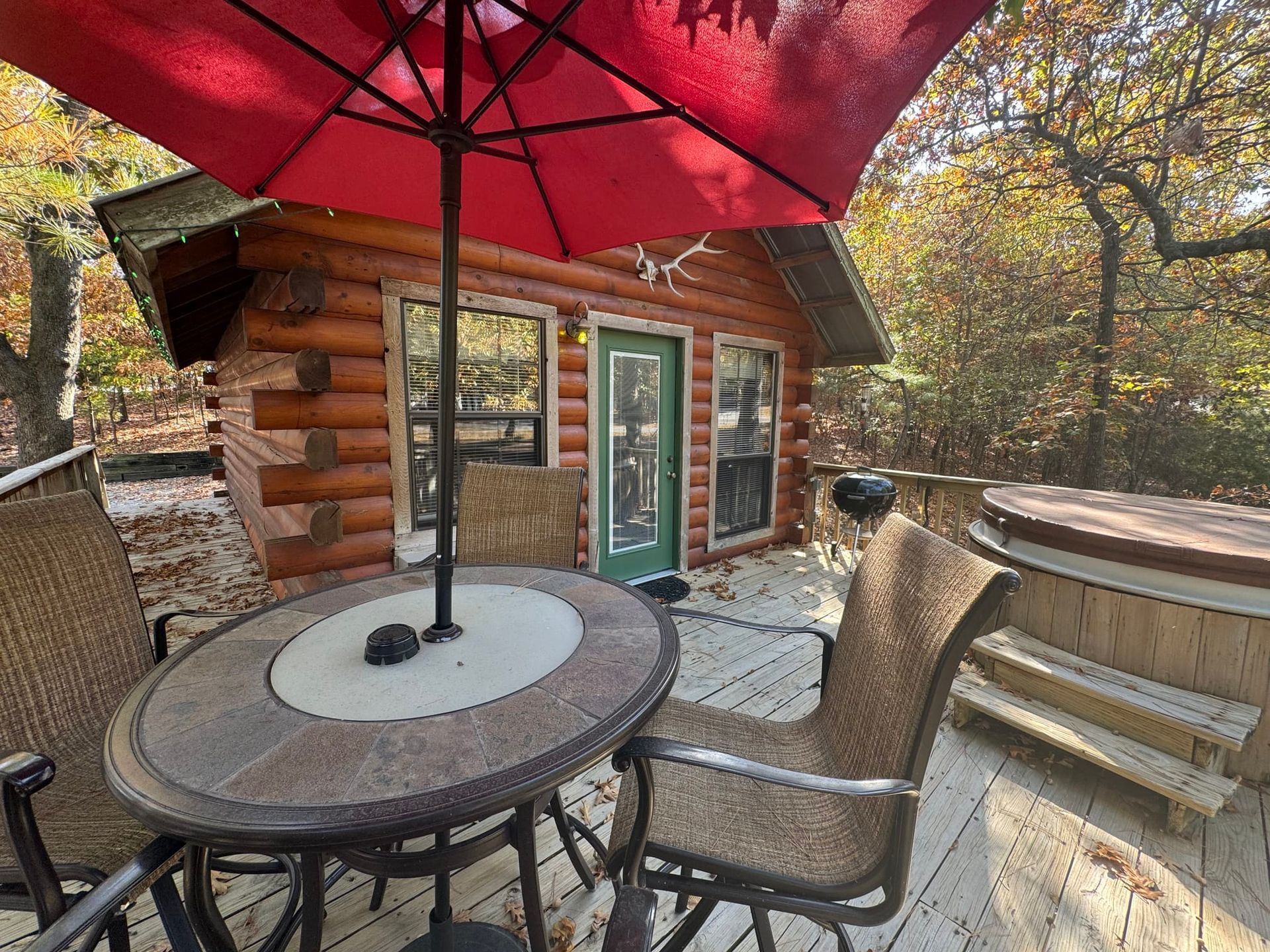 A table and chairs under an umbrella on a deck in front of a log cabin.
