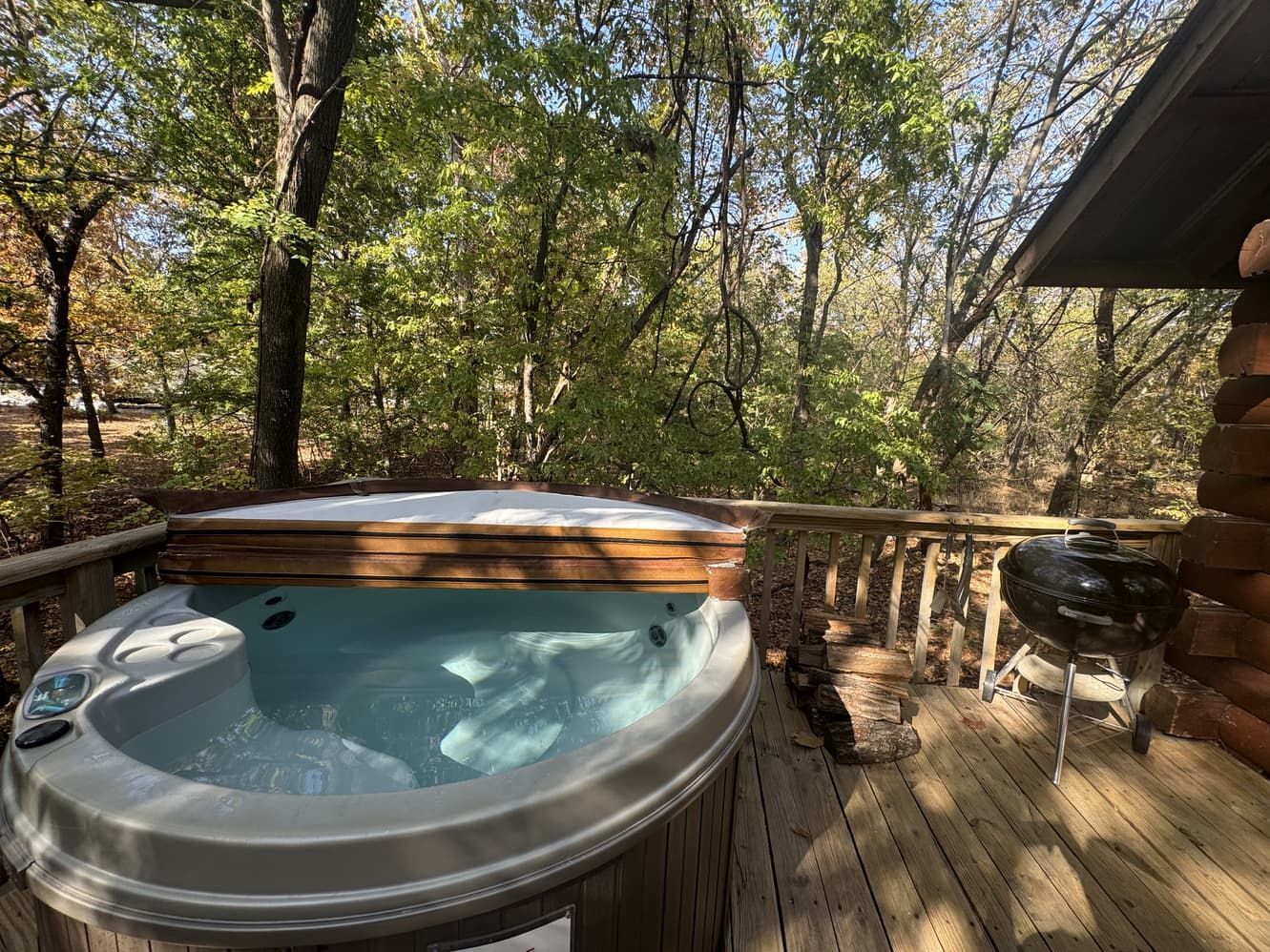 A hot tub is on a wooden deck next to a log cabin.
