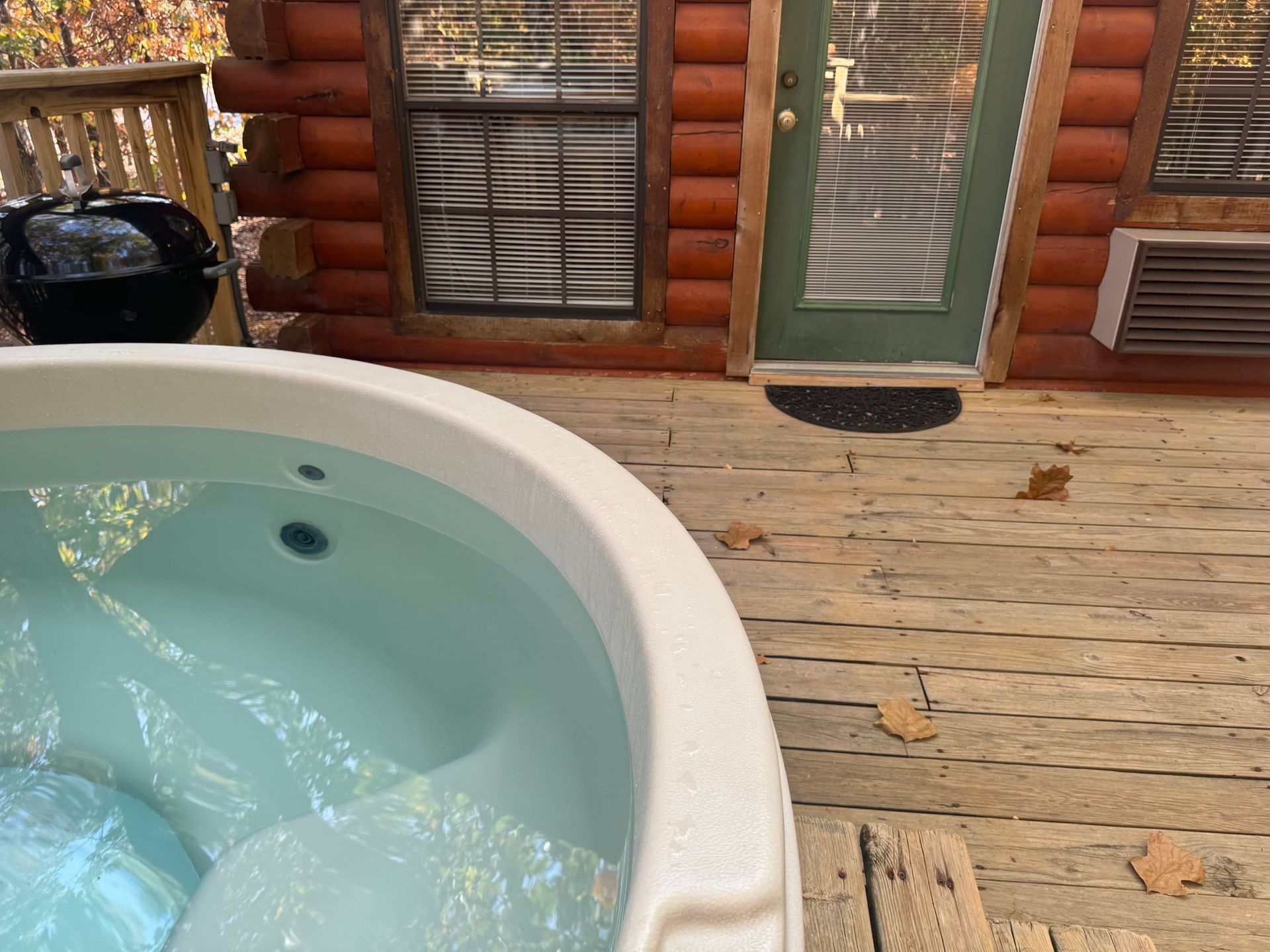 A hot tub is sitting on a wooden deck in front of a log cabin.