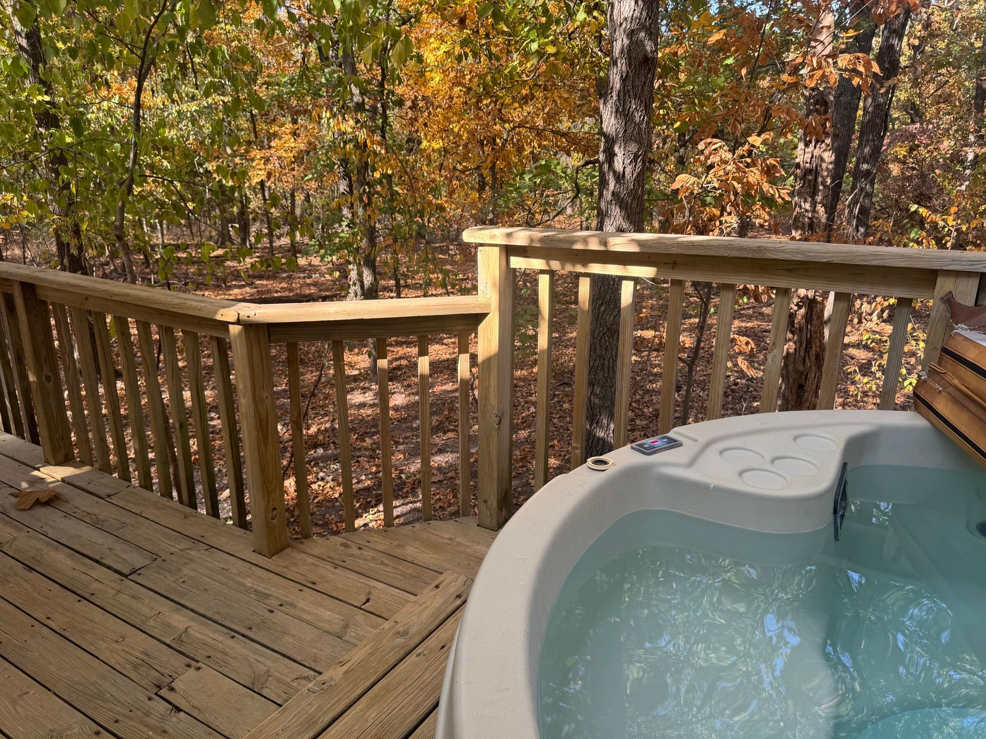 A hot tub is on a wooden deck with trees in the background.