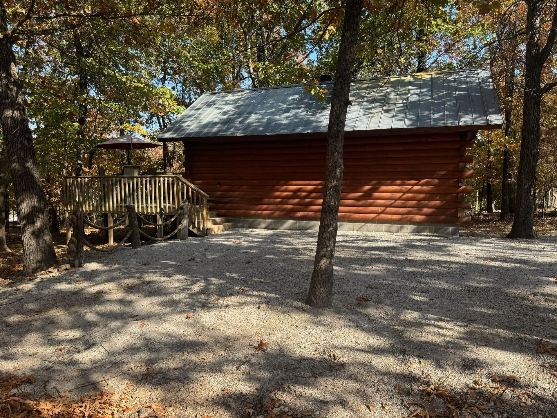 A log cabin is surrounded by trees and gravel in the woods.