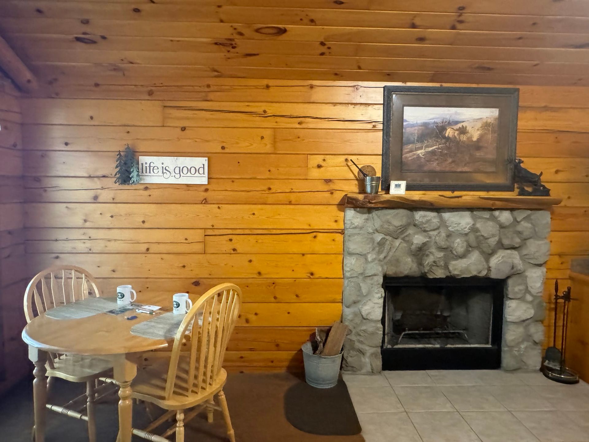 A wooden cabin with a stone fireplace and a table and chairs.