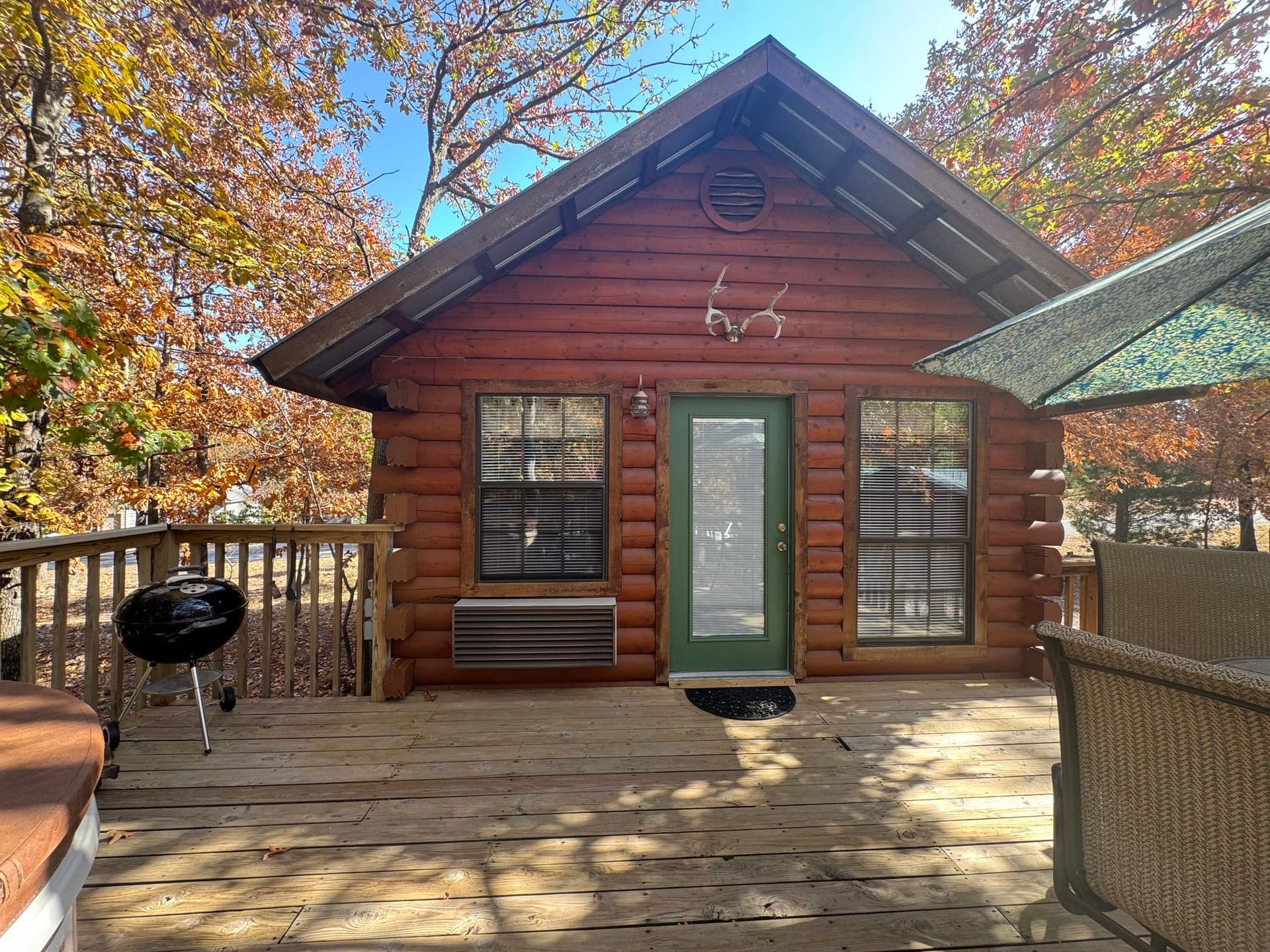 A small log cabin with a green door and a grill on the deck.