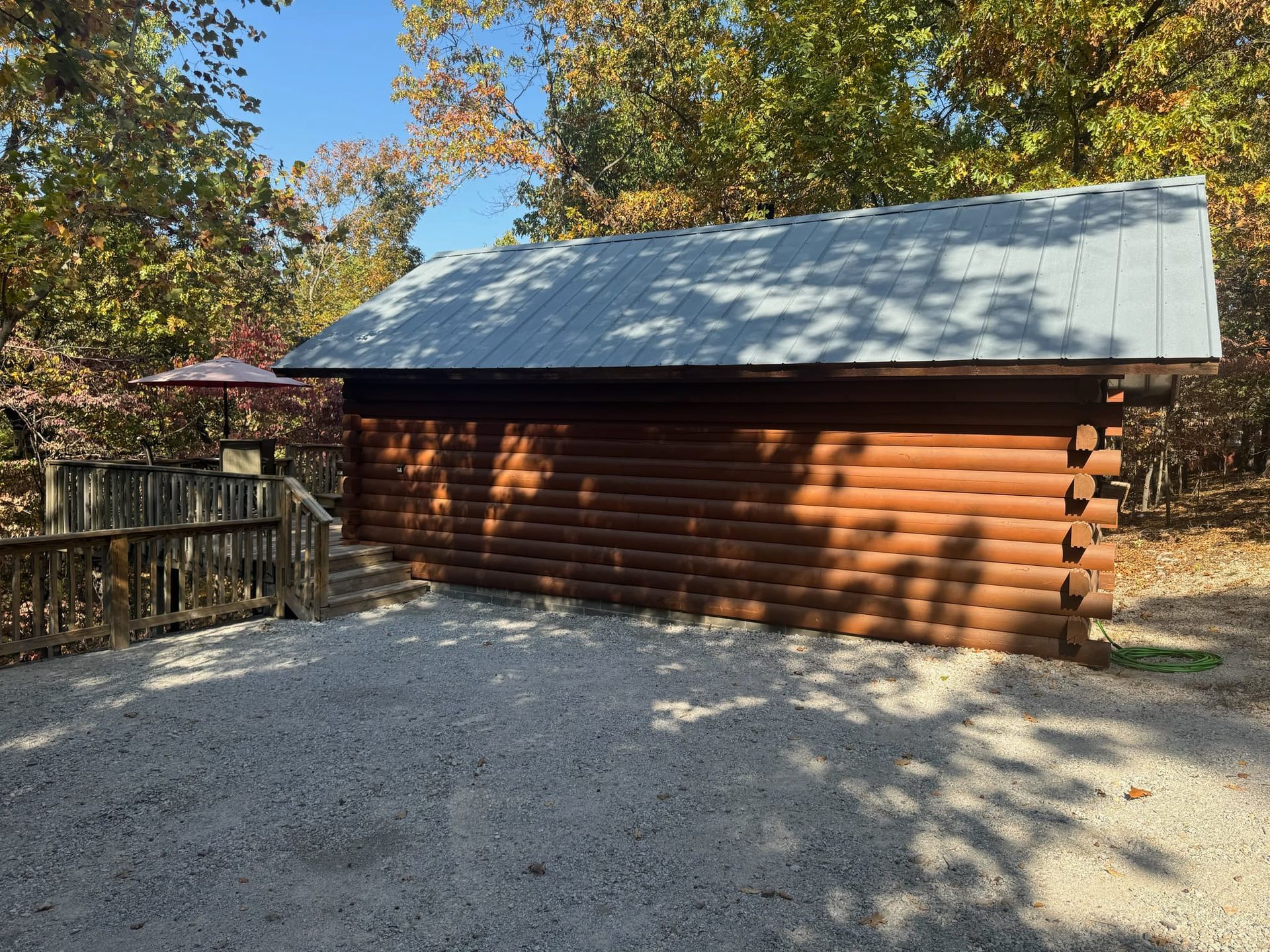 A log cabin is sitting in the middle of a gravel driveway surrounded by trees.