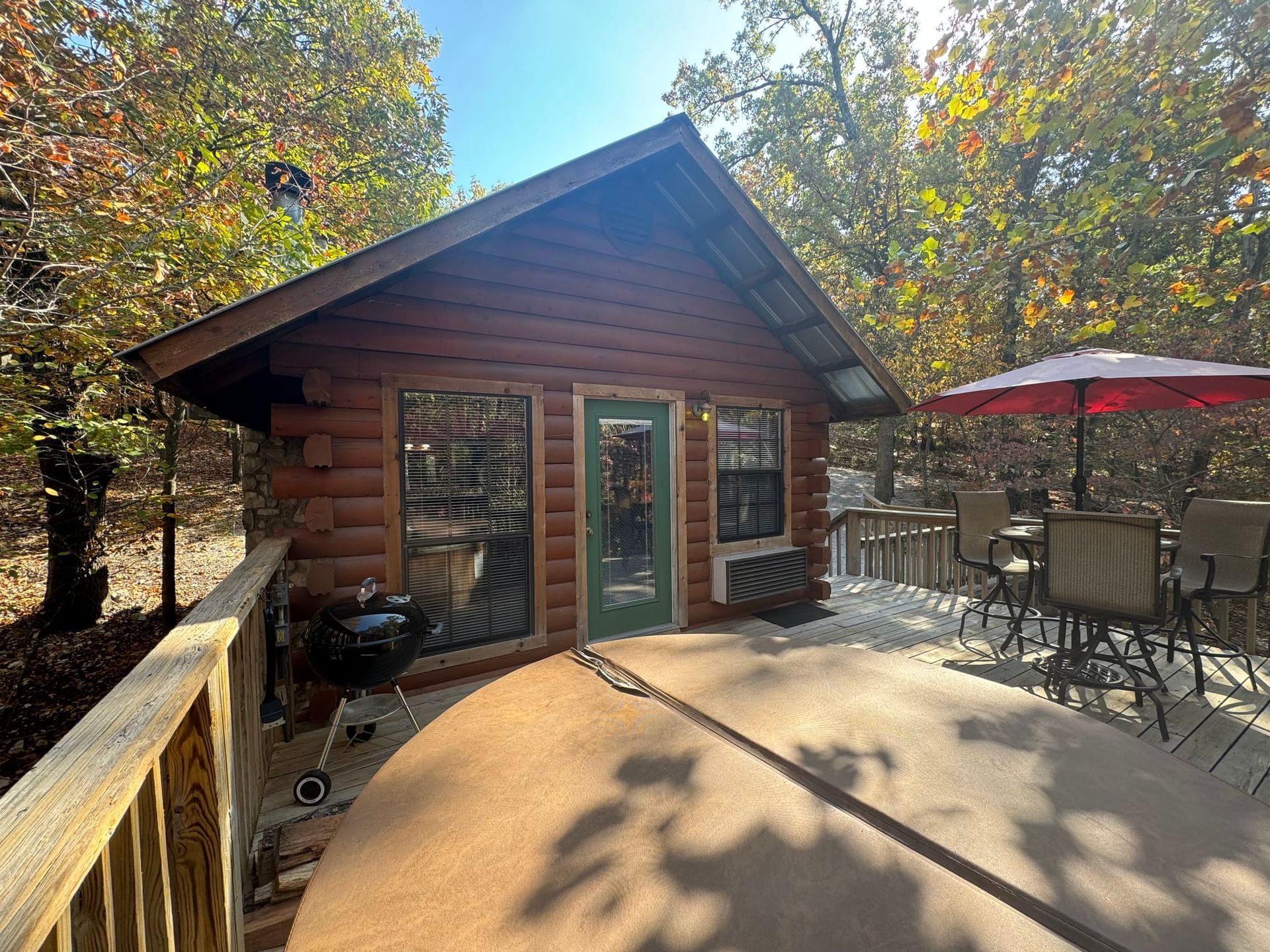 A small log cabin with a deck and umbrellas in the woods.