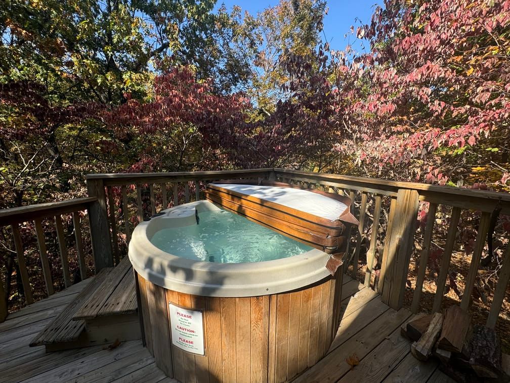 A hot tub is sitting on a wooden deck surrounded by trees.