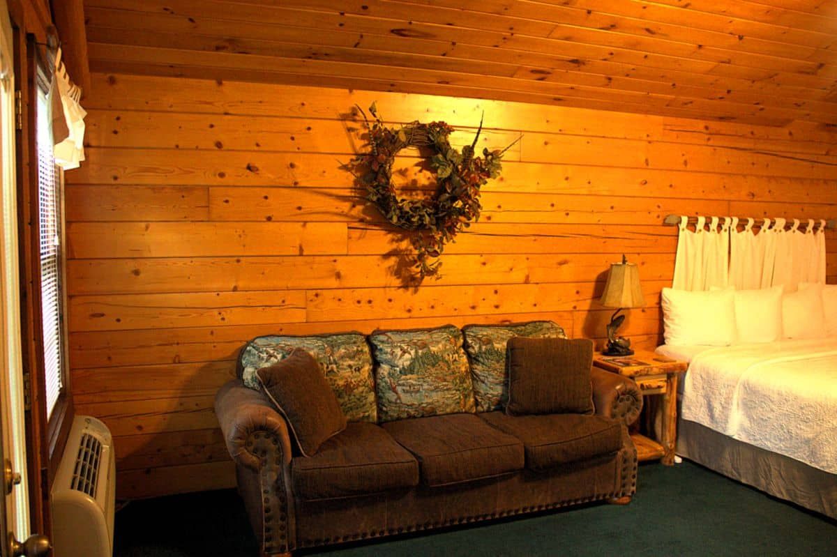 A living room with a couch and a bed in a log cabin.