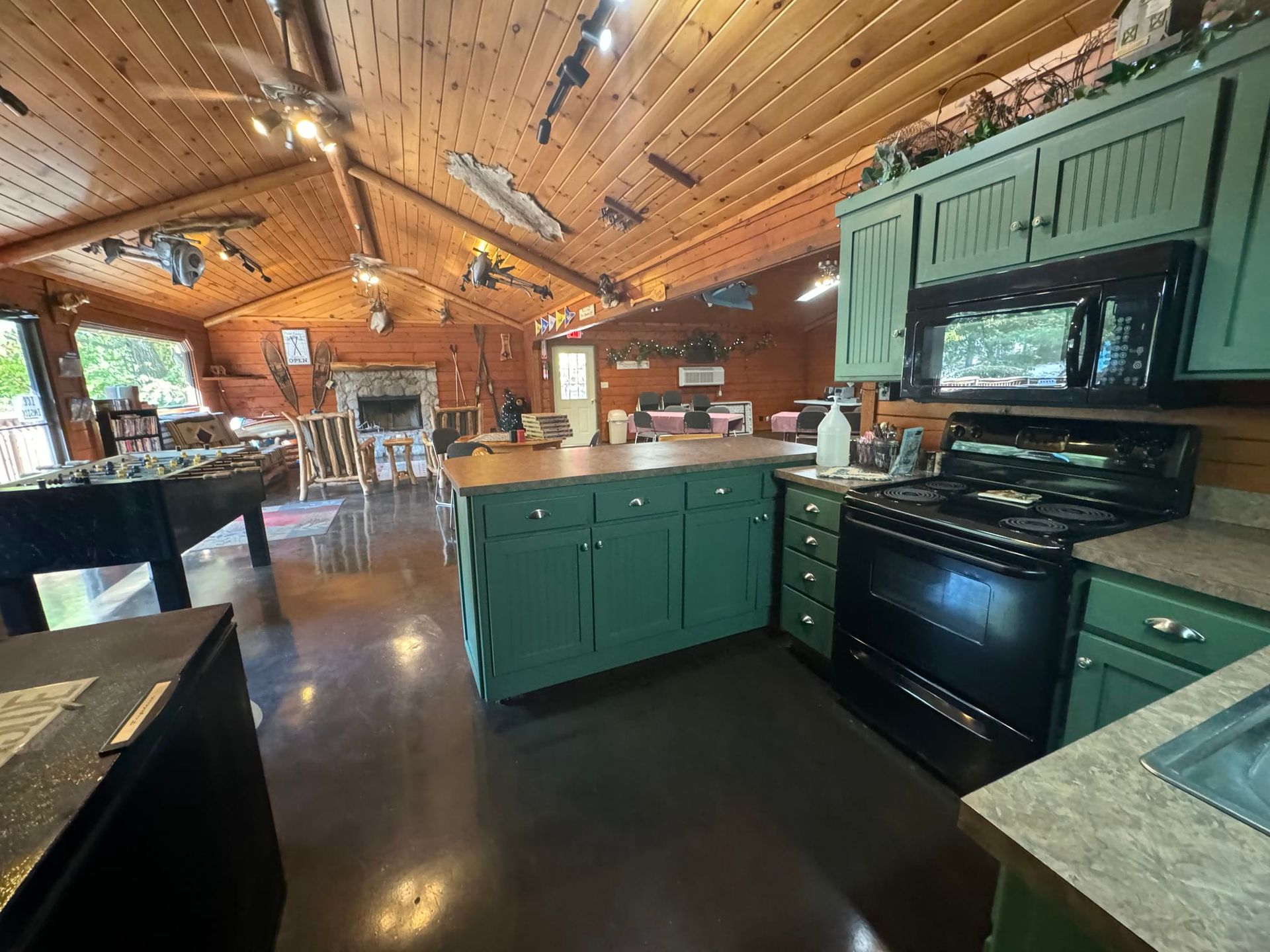 A kitchen with green cabinets , a stove , a microwave , and a pool table.