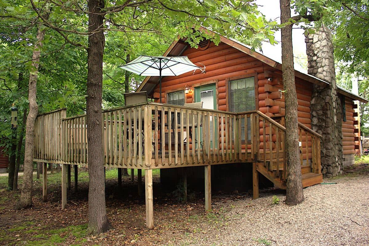 A log cabin with a large deck and umbrella in the woods.