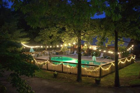 A swimming pool is lit up at night with string lights.